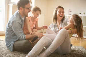 Eine Familie sitzt auf einem Teppich, tobt und lacht.